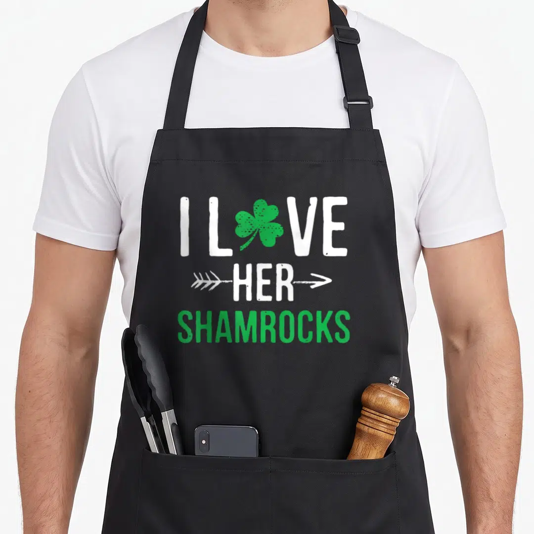 Couple st patrick day aprons - I Love Her Shamrocks text with green shamrock and white arrows — shown on a black cotton canvas apron against a white background