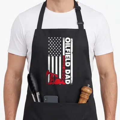 Oilfield field dad apron - Vertical distressed USA flag with red oil pumpjack and vertical OILFIELD DAD text — shown on a black cotton canvas apron against a white background