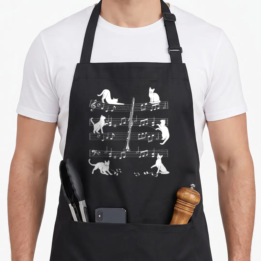 Clarinetist cat apron - Four white cats interacting with musical staffs and a vertical clarinet in line art — shown on a black cotton canvas apron against a white background