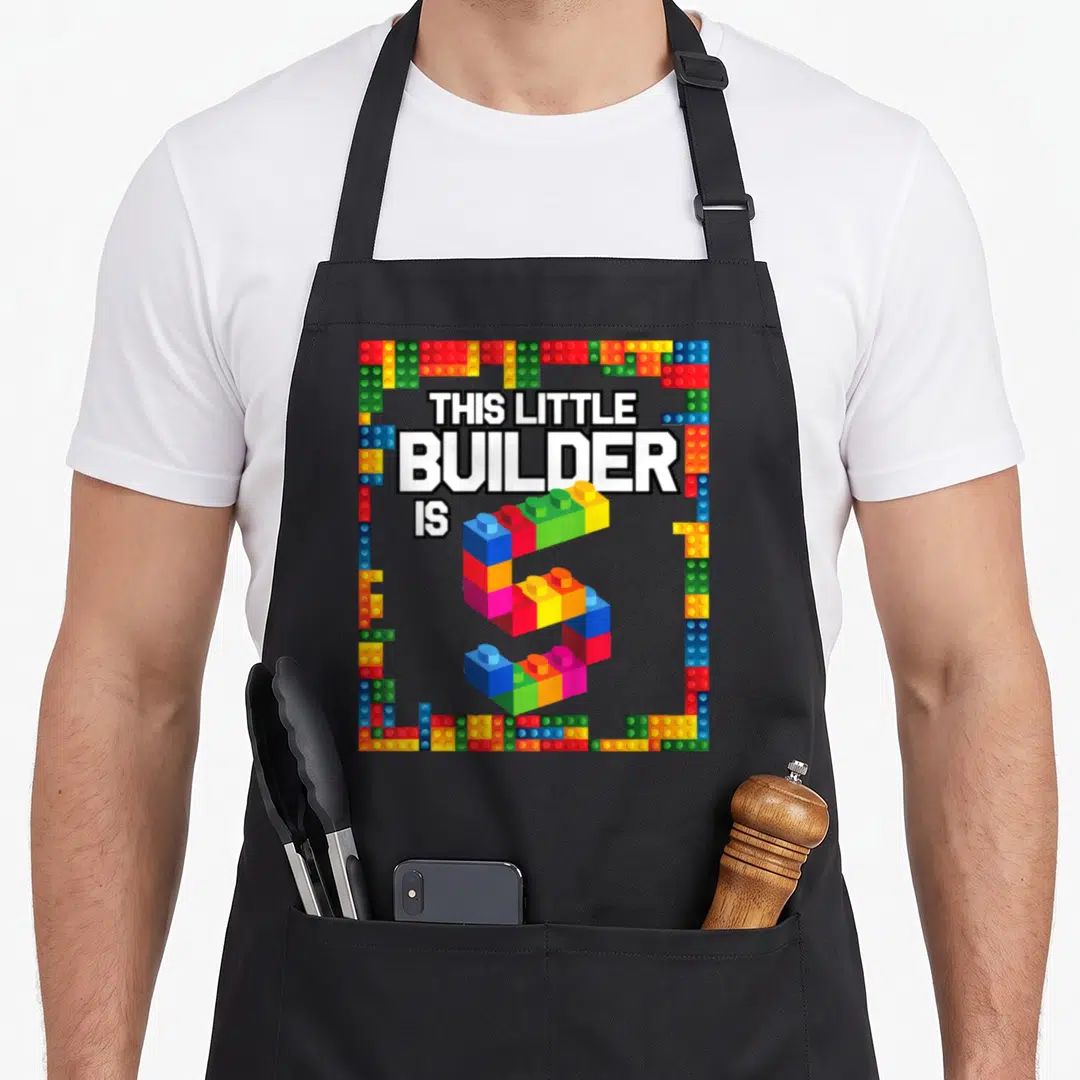 Birthday block & apron - Number 5 made of toy bricks with text This Little Builder Is surrounded by a brick border — shown on a black cotton canvas apron against a white background