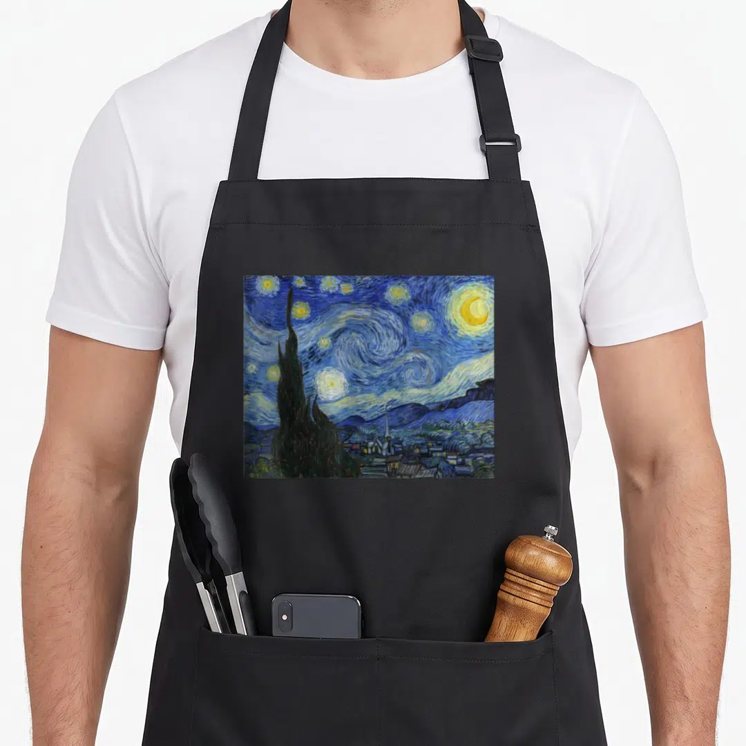 Starry van gogh apron - Swirling blue night sky with yellow stars, dark green cypress tree, and village below — shown on a black cotton canvas apron against a white background