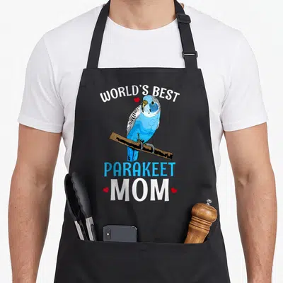 Budgy parakeet lover apron - Realistic blue parakeet perched on branch with WORLD'S BEST PARAKEET MOM text and red — shown on a black cotton canvas apron against a white background