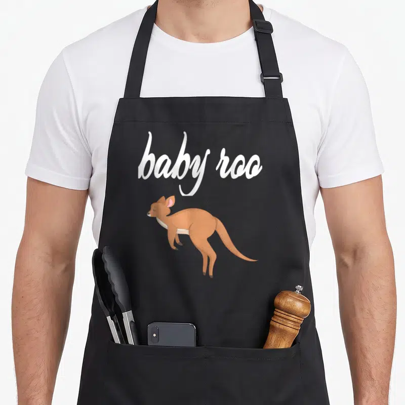 Baby kangaroo apron - White baby roo script above a brown cartoon joey kangaroo — shown on a black cotton canvas apron against a white background