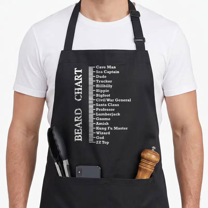 Measurement beard apron - Vertical white distressed text reading BEARD CHART next to a scale listing beard types — shown on a black cotton canvas apron against a white background