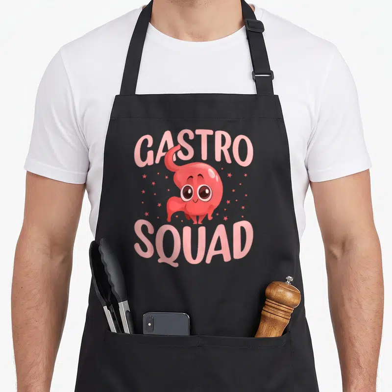 Medical assistant squad apron - Red cartoon stomach character centered between pink GASTRO SQUAD text with scattered — shown on a black cotton canvas apron against a white background