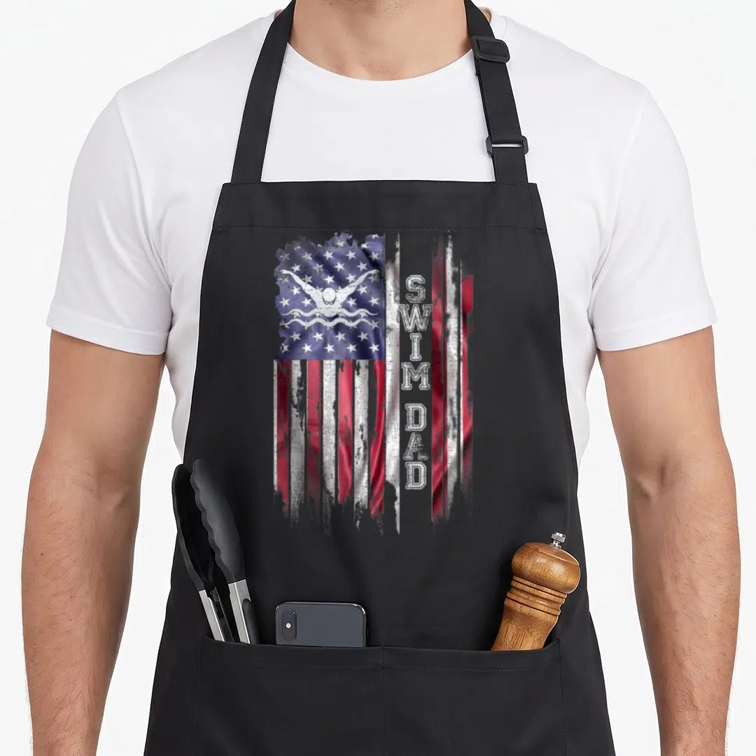 Flag swimming dad apron - Distressed US flag with white swimmer icon and vertical SWIM DAD text in red white blue — shown on a black cotton canvas apron against a white background