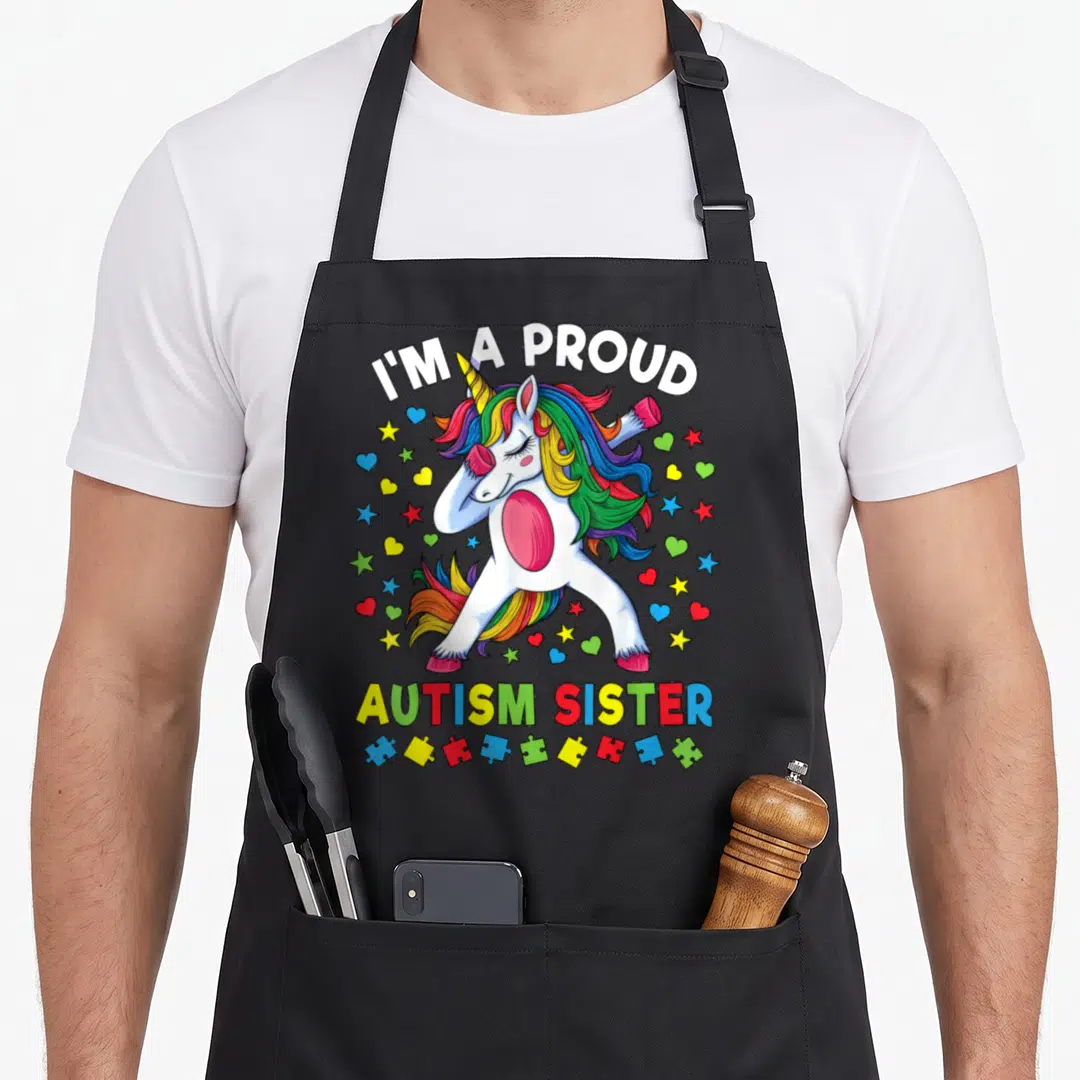 Proud unicorn apron - Dabbing unicorn with rainbow mane, puzzle pieces, and I'M A PROUD, AUTISM SISTER text — shown on a black cotton canvas apron against a white background