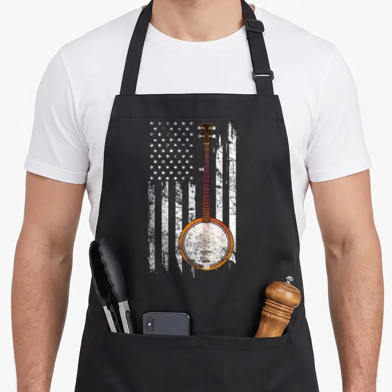 Bluegrass american flag apron - Distressed banjo centered over white and brown striped US flag pattern — shown on a black cotton canvas apron against a white background