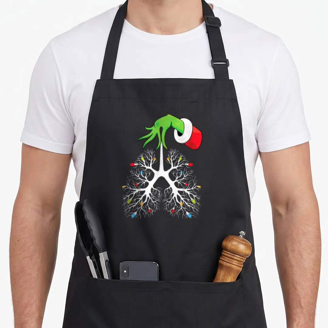 Nurse christmas lights apron - White lungs with colorful bulbs, green hand with red sleeve holding white tape — shown on a black cotton canvas apron against a white background