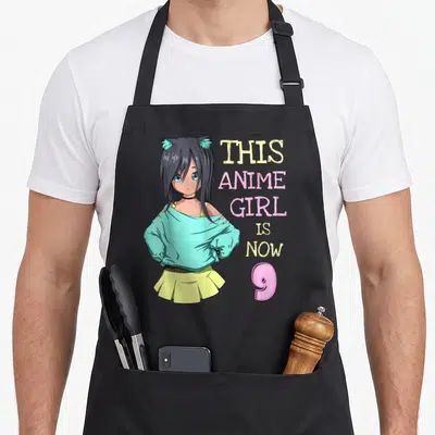 Vintage birthday anime mom apron - Anime girl with cat ears and text This Anime Girl Is Now 9 — shown on a black cotton canvas apron against a white background