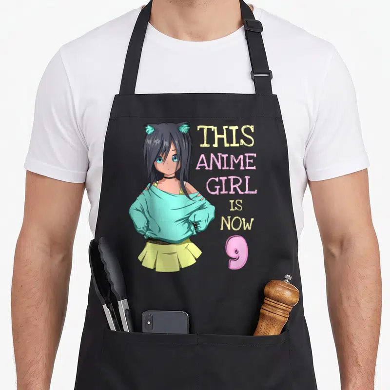 Vintage birthday anime mom apron - Anime girl with cat ears and text This Anime Girl Is Now 9 — shown on a black cotton canvas apron against a white background