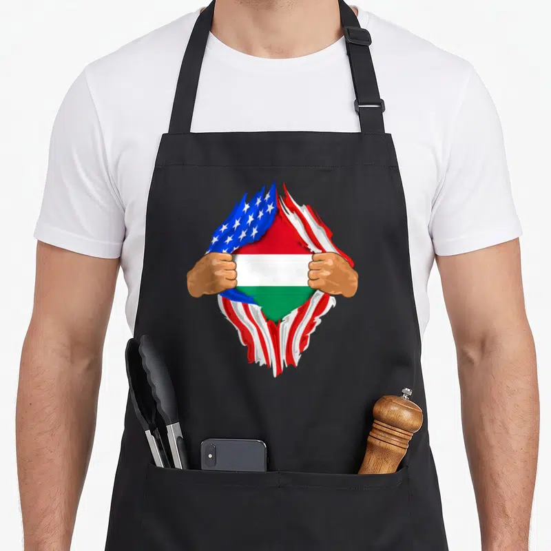 Hungarian blood apron - Two brown hands tear red white and blue USA flag revealing red white green Hungarian flag — shown on a black cotton canvas apron against a white background