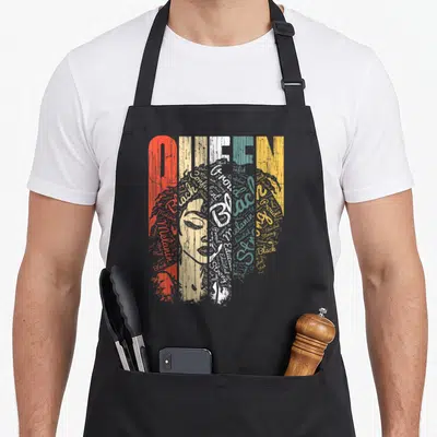Queen african apron - Distressed QUEEN text and woman portrait formed by words Black Proud Strong Educated Confident — shown on a black cotton canvas apron against a white background