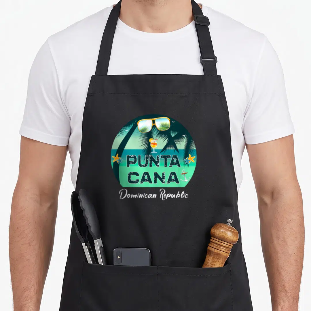 Dominican punta cana apron - Retro circular beach scene with sunglasses, cocktail, palm trees, PUNTA CANA text — shown on a black cotton canvas apron against a white background