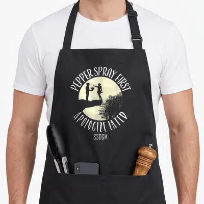 Pepper spritz apron - PEPPER SPRAY FIRST APOLOGIZE LATER couple silhouette cliff moon SSDGM — shown on a black cotton canvas apron against a white background