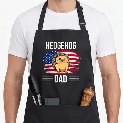 Hedgehog father day apron - Cartoon hedgehog on red white blue brush stroke flag with HEDGEHOG DAD text — shown on a black cotton canvas apron against a white background