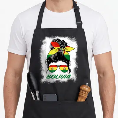 Bleached bolivian girl apron - Woman silhouette with bun, flag sunglasses, and BOLIVIA text on white splatter — shown on a black cotton canvas apron against a white background