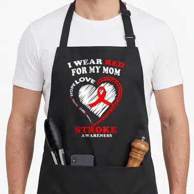 Stroke pink ribbon apron - Red and white heart with ribbon and text I Wear Red For My Mom Stroke Awareness — shown on a black cotton canvas apron against a white background