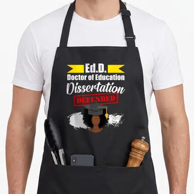 Edd education apron - Ed.D. Dissertation Defended text above graduate in cap with white paint stroke — shown on a black cotton canvas apron against a white background