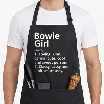 Bowie texas apron - White typography defining Bowie Girl as a loving, sassy person — shown on a black cotton canvas apron against a white background