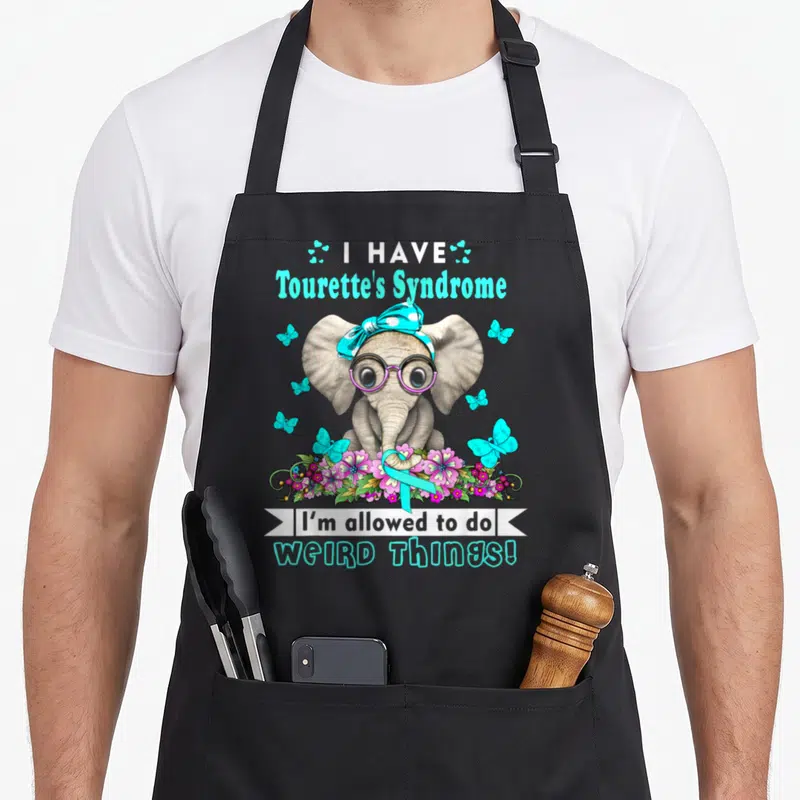 Vintage syndrome tourette awareness apron - Elephant in glasses and bandana surrounded by butterflies, flowers, ribbon — shown on a black cotton canvas apron against a white background