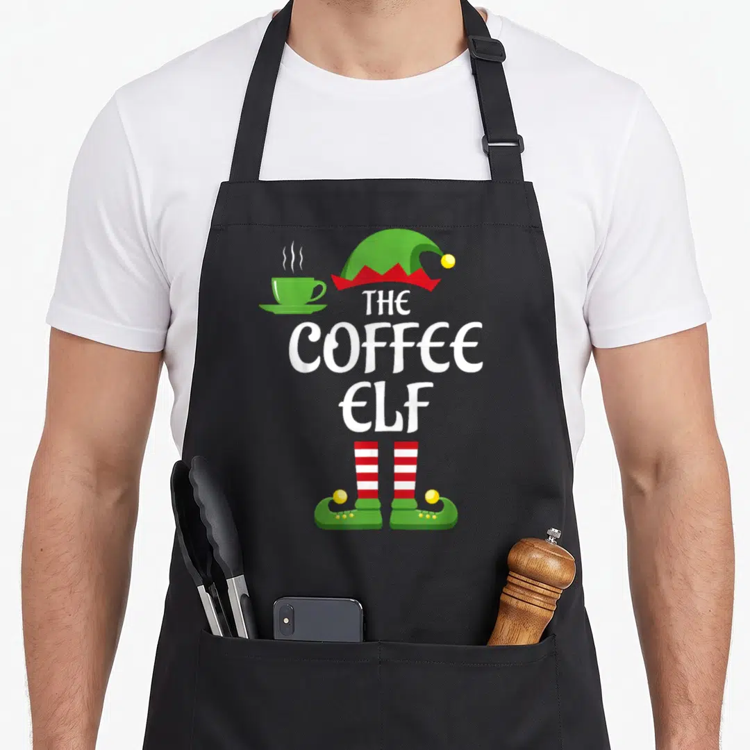 Coffee christmas elf apron - Green elf hat, white stacked text, red striped socks, green shoes, and steaming green — shown on a black cotton canvas apron against a white background
