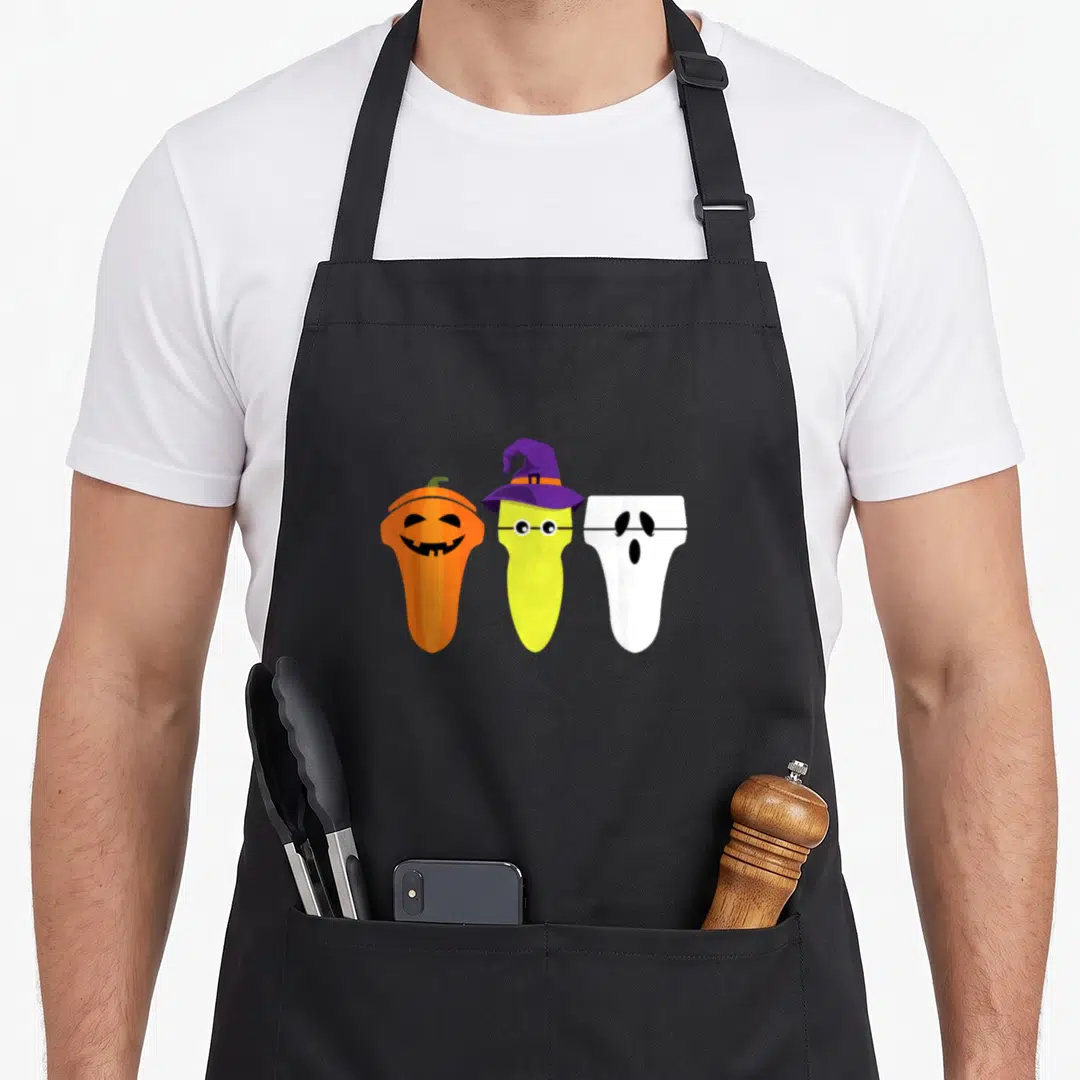 Sonographer halloween witch apron - Three cartoon transducers dressed as an orange pumpkin, a yellow witch, and a white — shown on a black cotton canvas apron against a white background