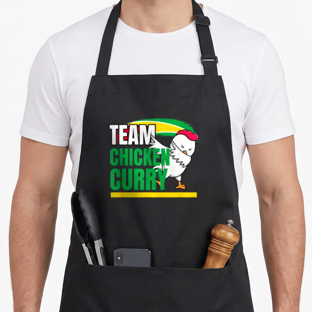 Caribbean patriotic apron - Stacked TEAM CHICKEN CURRY text with cartoon chicken and green yellow red brush strokes — shown on a black cotton canvas apron against a white background