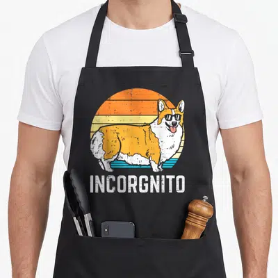 Incorgnito corgi aprons - Retro corgi in sunglasses before striped sun with INCORGNNITO text below — shown on a black cotton canvas apron against a white background