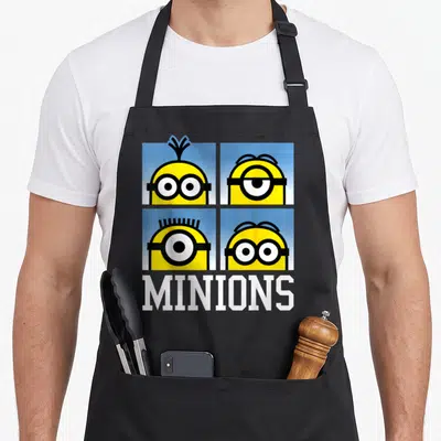 Bust general apron - Four yellow minion heads in blue squares above white MINIONS text — shown on a black cotton canvas apron against a white background