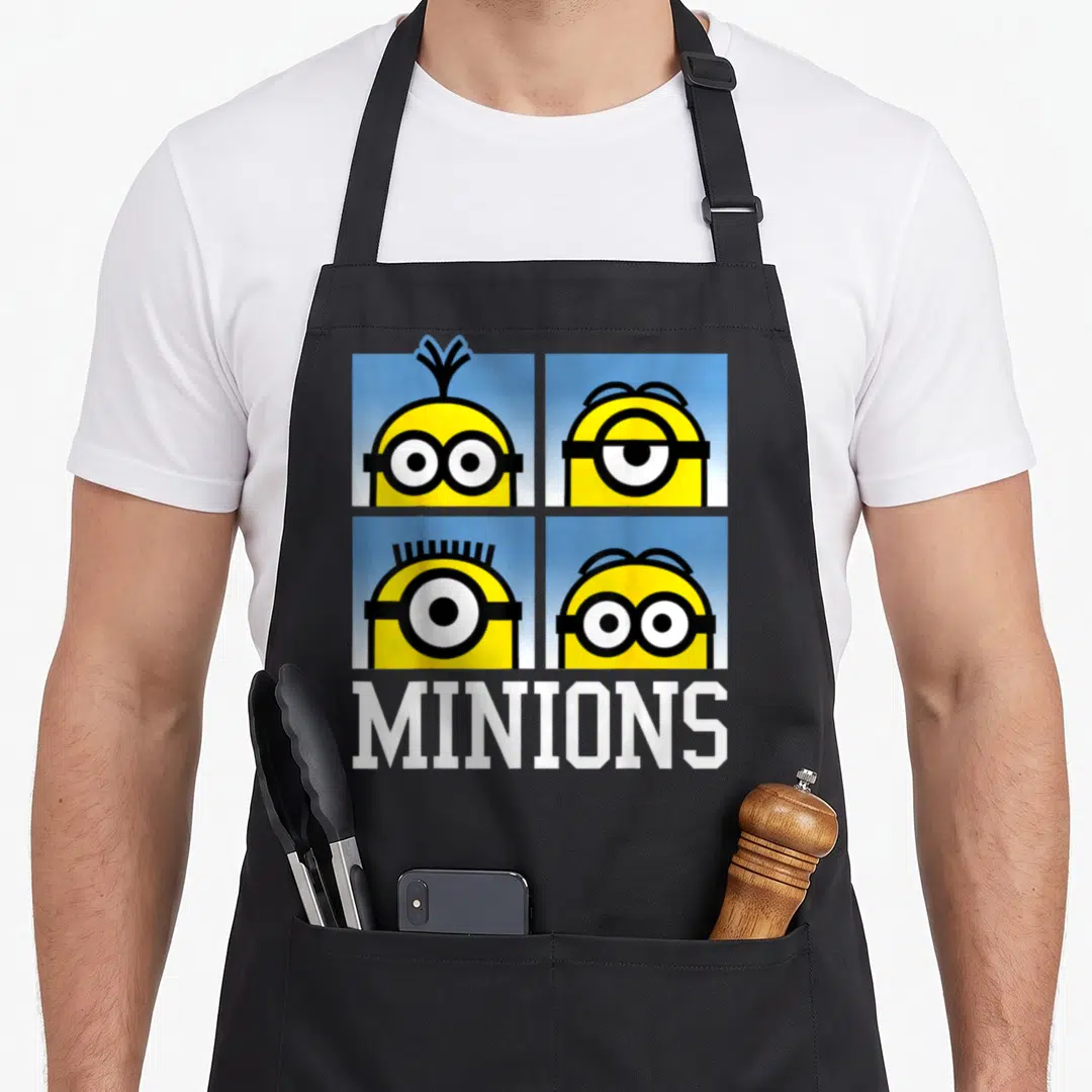 Bust general apron - Four yellow minion heads in blue squares above white MINIONS text — shown on a black cotton canvas apron against a white background