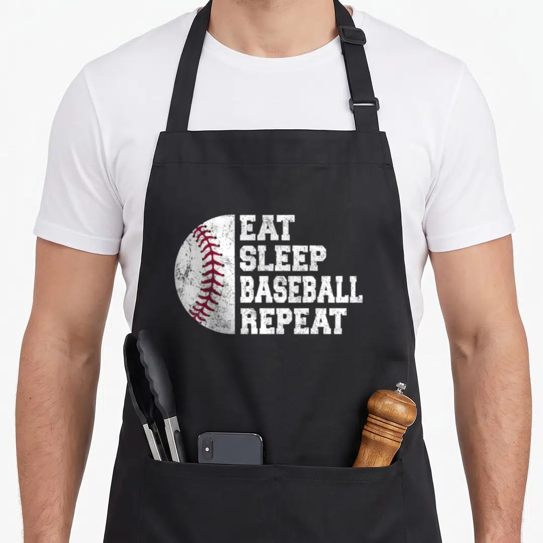 Repeat baseball apron - Distressed white text EAT SLEEP BASEBALL REPEAT beside a half baseball with red stitching — shown on a black cotton canvas apron against a white background