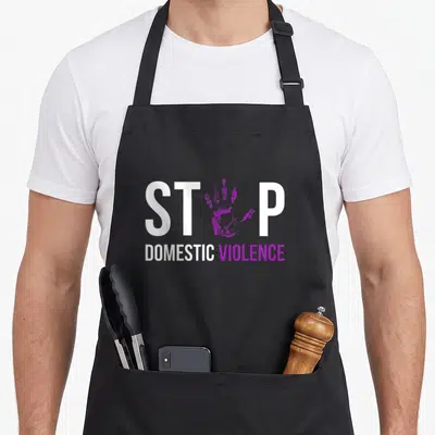 Stop violence domestic aprons - Purple handprint between white ST and P letters above DOMESTIC VIOLENCE text — shown on a black cotton canvas apron against a white background