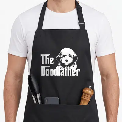Labradoodle dog apron - White minimalist dog head next to The Doodfather text — shown on a black cotton canvas apron against a white background