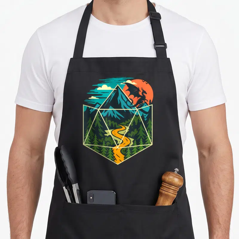 D20 dice game aprons - Dragon silhouette over mountains and river inside a hexagonal frame with blue green orange colors — shown on a black cotton canvas apron against a white background