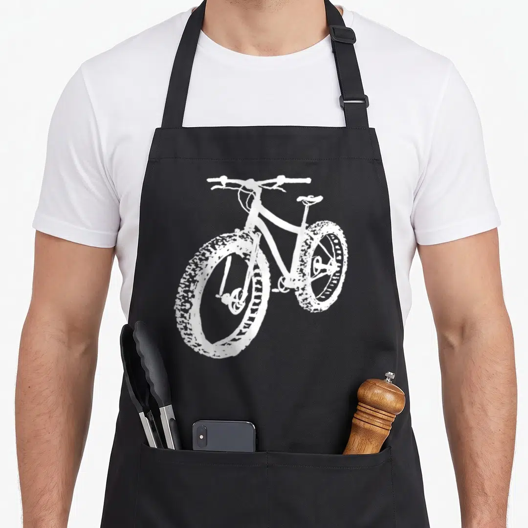 Tire fat man in apron - White line-art fat bike with wide knobby tires on black fabric — shown on a black cotton canvas apron against a white background