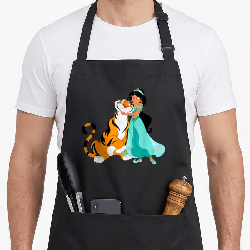 Jasmine princess apron - Cartoon princess in turquoise dress hugging a large orange and black tiger — shown on a black cotton canvas apron against a white background
