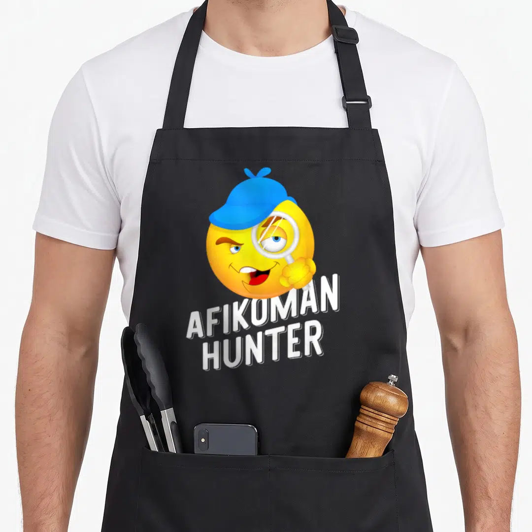 Hunter passover apron - Yellow smiley face in blue hat holding magnifying glass above white AFIKOMAN HUNTER text — shown on a black cotton canvas apron against a white background
