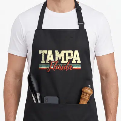 Cute tampa florida apron - TAMPA Florida distressed text over teal beige red horizontal stripes — shown on a black cotton canvas apron against a white background