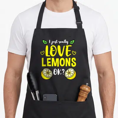Retro lemon apron - Stacked yellow text I just really LOVE LEMONS OK with two green leaves, two hearts, and two lemon — shown on a black cotton canvas apron against a white background