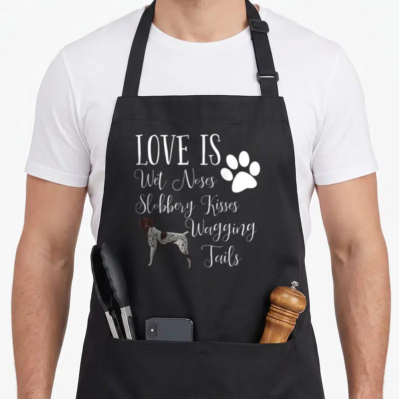 Shorthair dog pointer apron - White stacked text reading Love Is Wet Noses next to a brown and white spotted dog — shown on a black cotton canvas apron against a white background