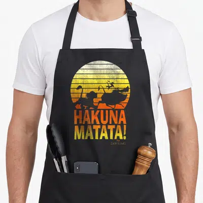 Hakuna distressed apron - Retro striped sunset with grey animal silhouettes and stacked HAKUNA MATATA text — shown on a black cotton canvas apron against a white background