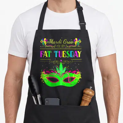 Mask fat chef apron - Mardi Gras and Fat Tuesday text with three masquerade masks and swirls in green purple yellow — shown on a black cotton canvas apron against a white background