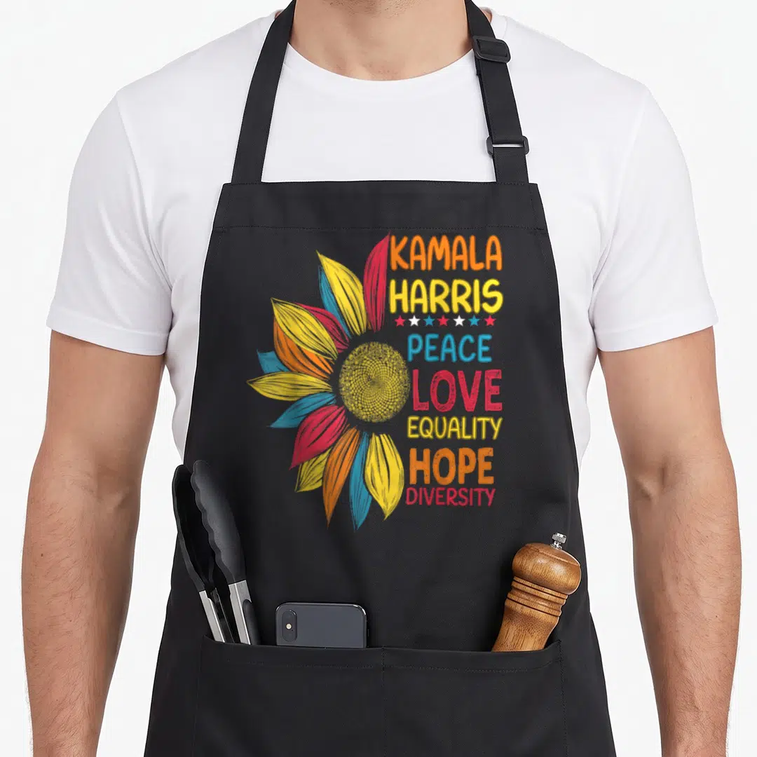 Kamala peace apron - Sunflower with KAMALA HARRIS text and stacked values in yellow orange red blue — shown on a black cotton canvas apron against a white background