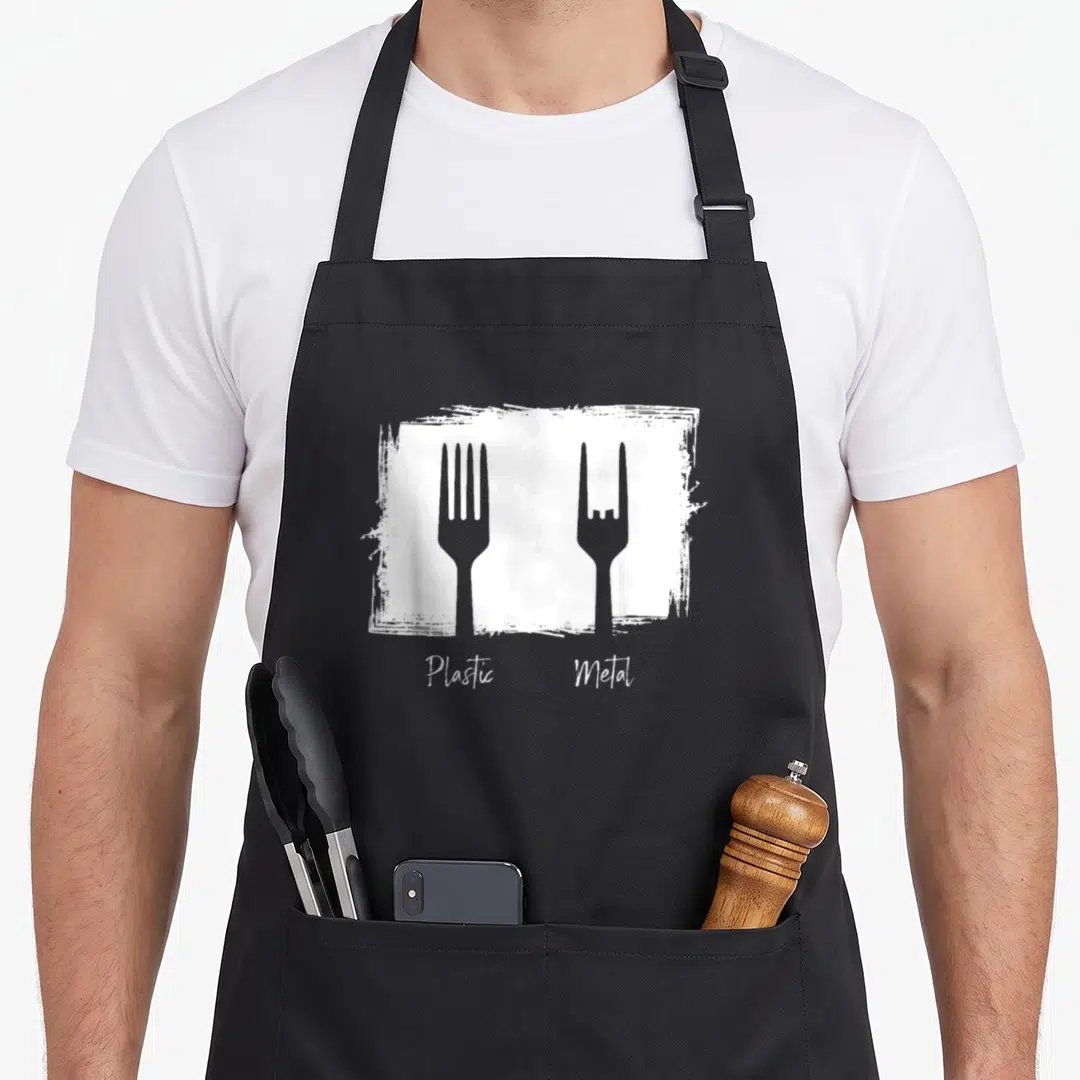 Rocker heavy apron - Plastic Metal text below standard and rock-sign forks in white distressed box — shown on a black cotton canvas apron against a white background