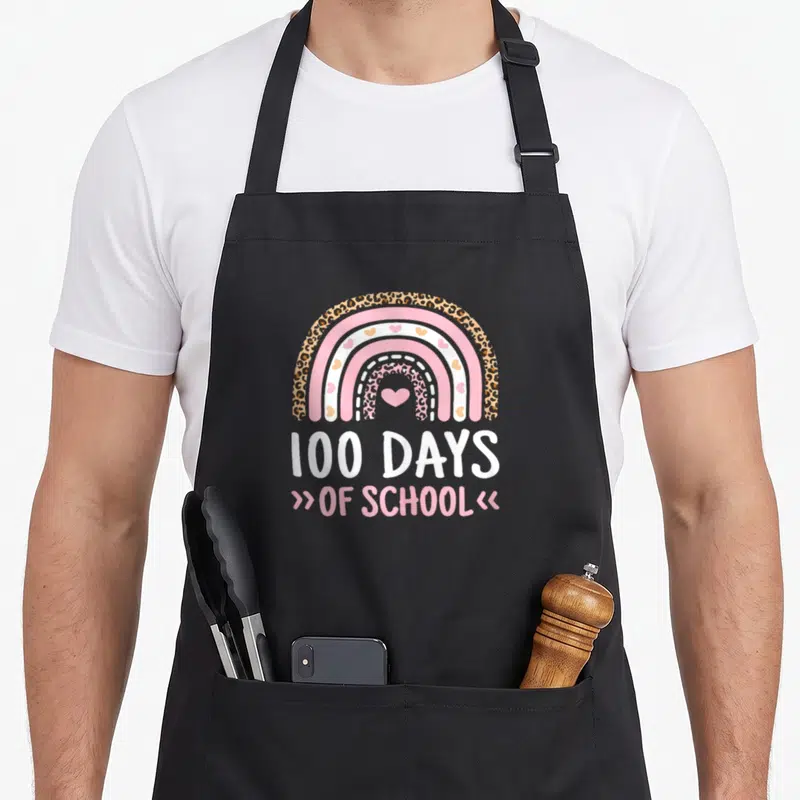 School 100th rainbow apron - Leopard print rainbow with hearts and 100 DAYS OF SCHOOL text in pink and white — shown on a black cotton canvas apron against a white background
