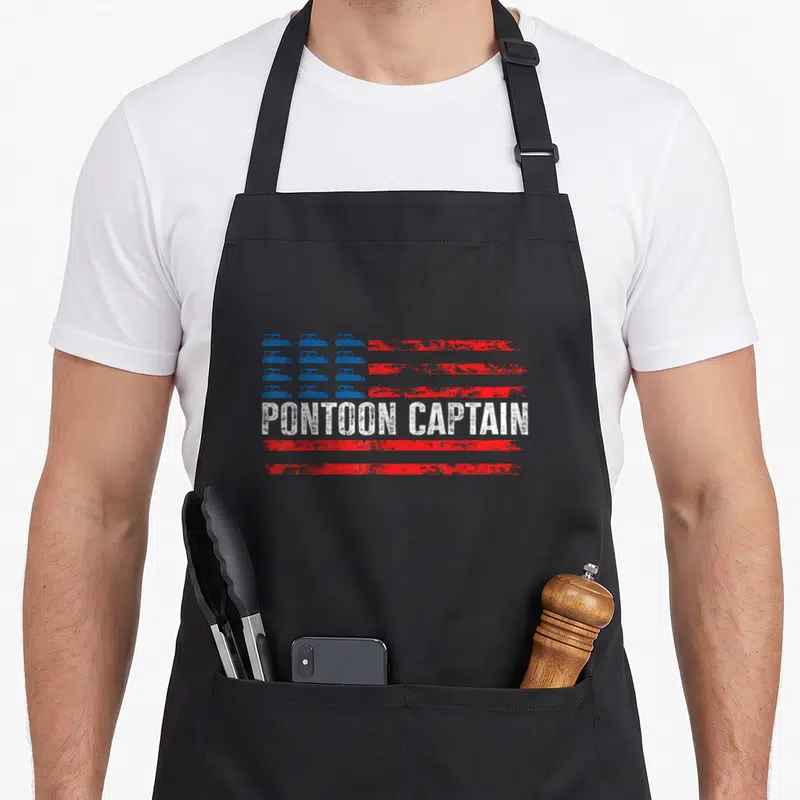 Boating 4th of july apron - PONTONE CAPTAIN text over red stripes with blue pontoon boat grid on left — shown on a black cotton canvas apron against a white background