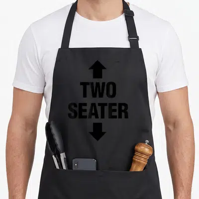 Seater dirty addict apron - Stacked black text TWO SEATER with upward and downward arrows — shown on a black cotton canvas apron against a white background