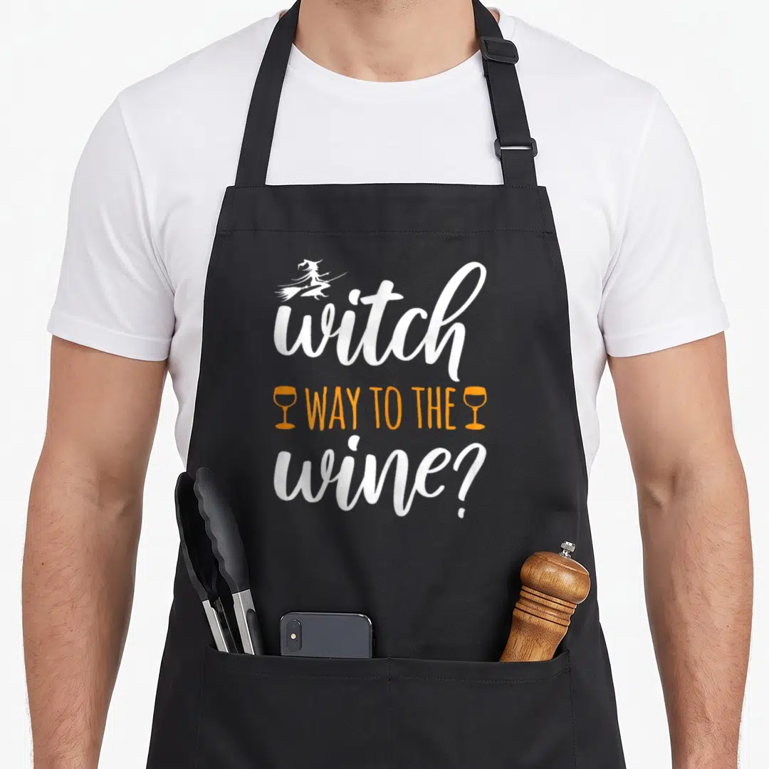 Witch wine aprons - Witch on broom with text witch way to the wine in white and orange script — shown on a black cotton canvas apron against a white background