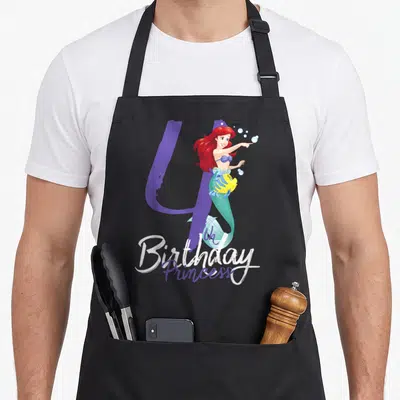 Ariel princess apron - Mermaid pointing next to purple number 4 and yellow fish with Birthday Princess text — shown on a black cotton canvas apron against a white background